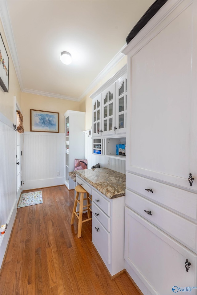 kitchen featuring crown molding, stone countertops, glass insert cabinets, white cabinetry, and light wood-type flooring