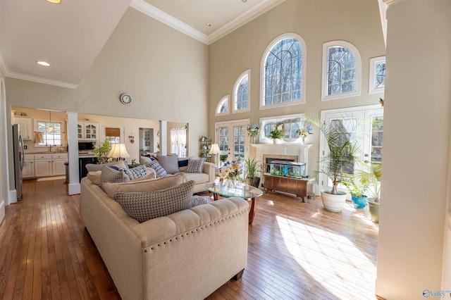 living area with ornamental molding, a glass covered fireplace, decorative columns, and wood finished floors