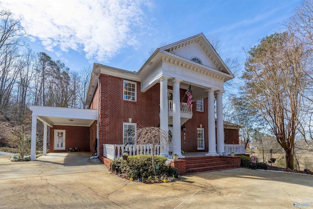 neoclassical home with driveway, covered porch, a carport, and brick siding