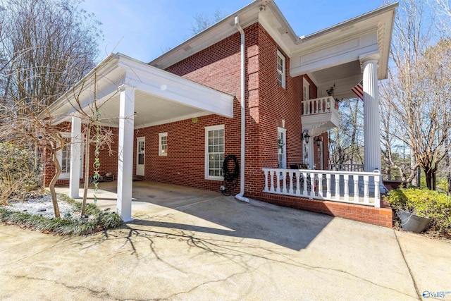 exterior space with brick siding, covered porch, a balcony, a carport, and driveway