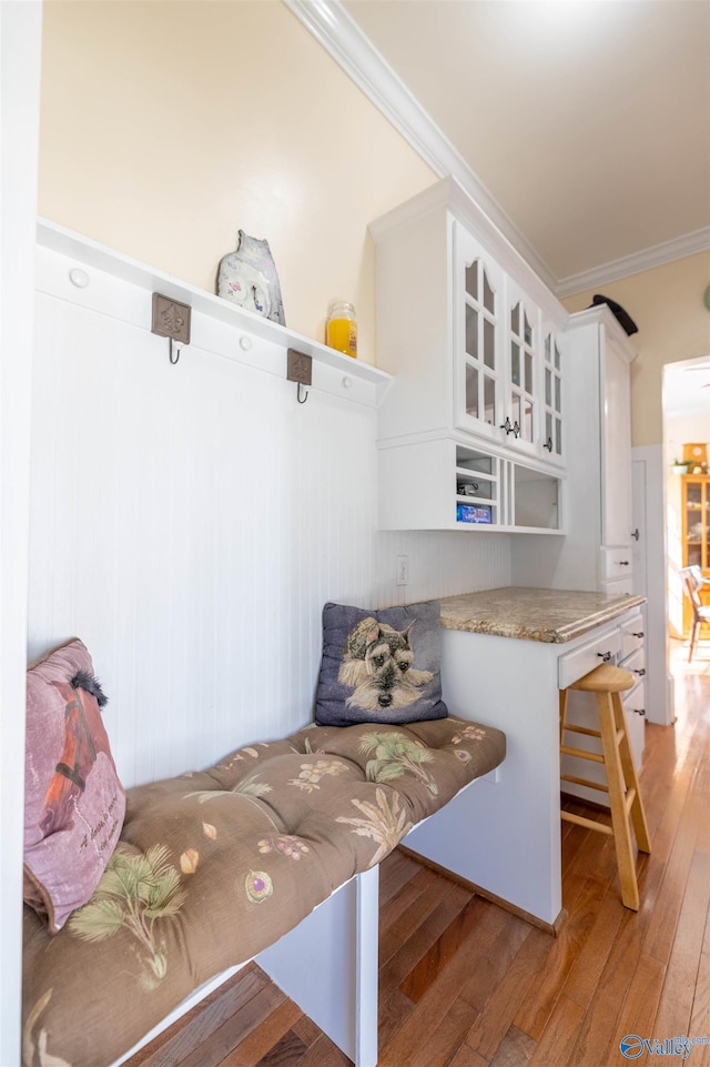 kitchen featuring glass insert cabinets, wood finished floors, crown molding, a kitchen bar, and white cabinetry