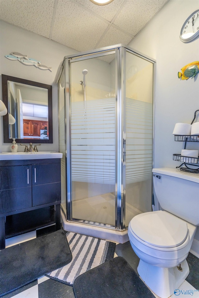 full bathroom featuring a drop ceiling, a shower stall, toilet, and vanity