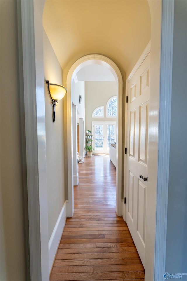 hall with light wood finished floors, baseboards, and arched walkways