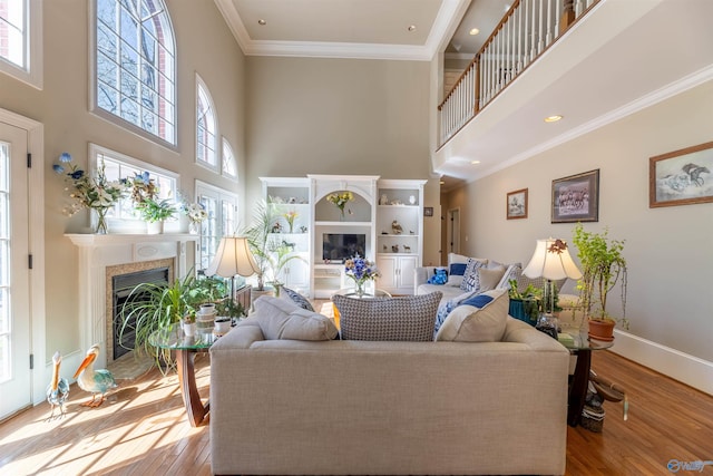 living room with light wood-style flooring, a high ceiling, a fireplace, baseboards, and ornamental molding