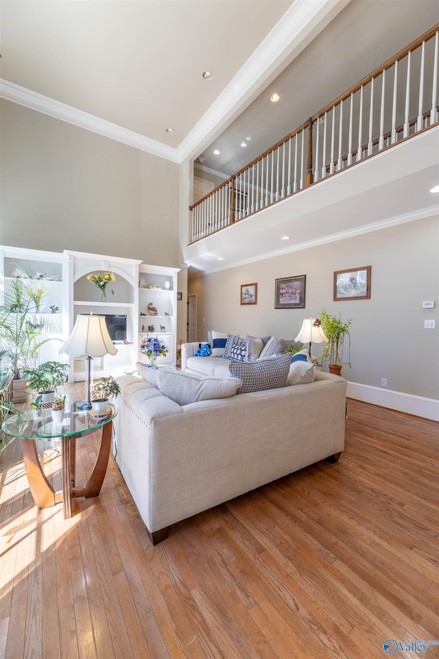 living area featuring light wood finished floors, baseboards, a glass covered fireplace, ornamental molding, and a high ceiling