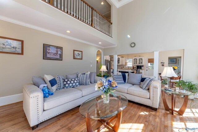 living room featuring ornamental molding, arched walkways, baseboards, and wood finished floors