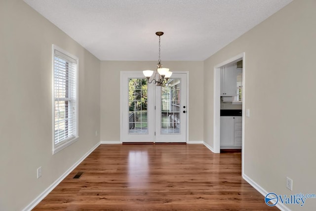 unfurnished dining area featuring dark hardwood / wood-style flooring, a textured ceiling, and a chandelier