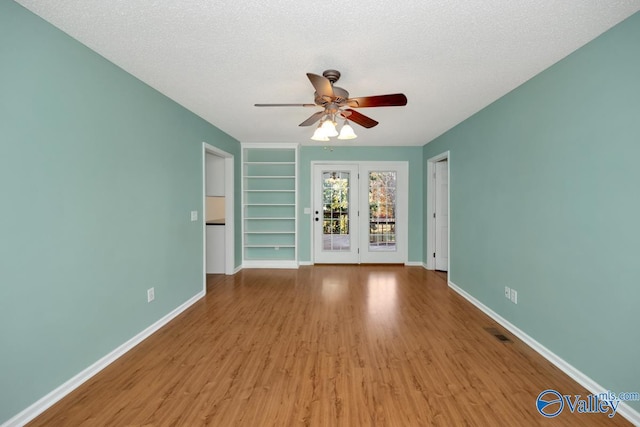 unfurnished room with ceiling fan, light hardwood / wood-style flooring, a textured ceiling, and built in shelves