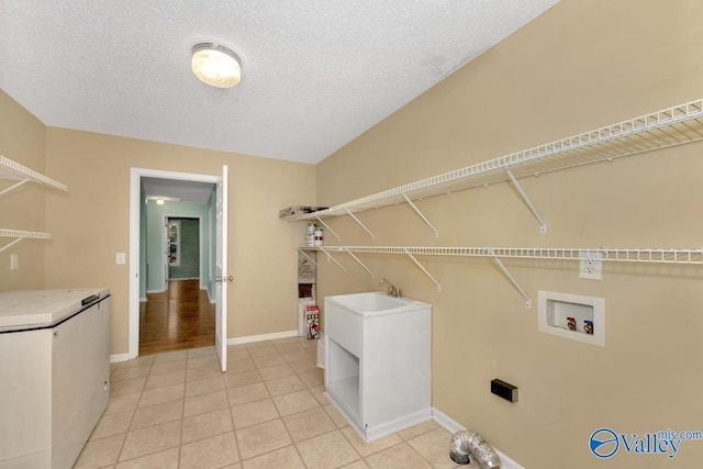 laundry area with light tile patterned floors, hookup for a washing machine, sink, and a textured ceiling