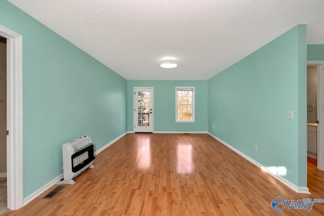 unfurnished living room with heating unit, a textured ceiling, and light wood-type flooring