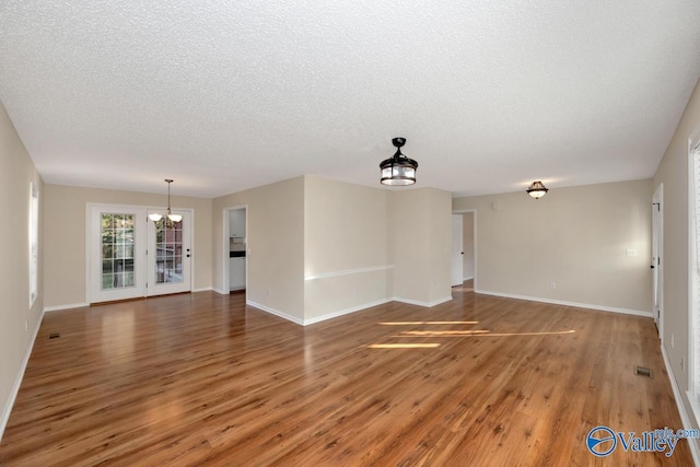 unfurnished living room featuring an inviting chandelier, dark hardwood / wood-style floors, and a textured ceiling