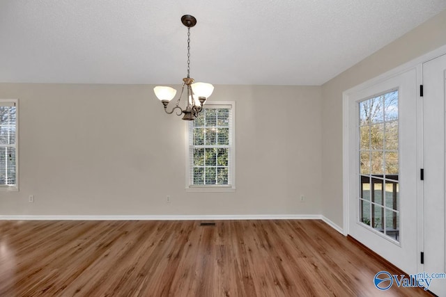 unfurnished dining area featuring hardwood / wood-style flooring, plenty of natural light, a textured ceiling, and an inviting chandelier