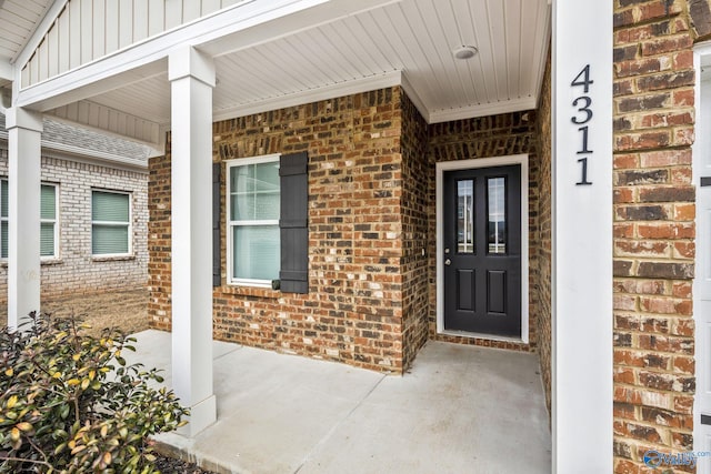 view of exterior entry with brick siding, board and batten siding, and a porch