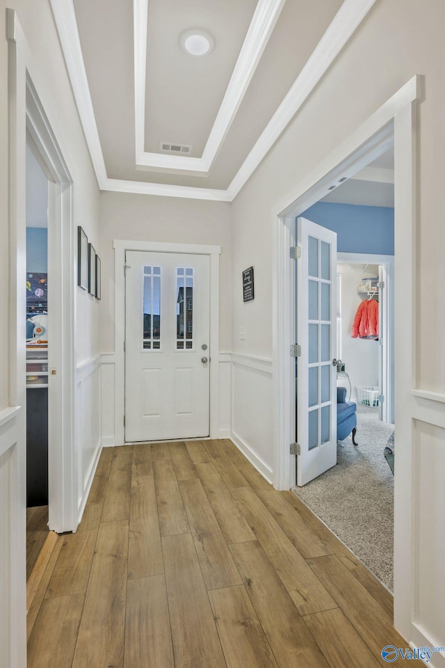 doorway to outside with ornamental molding, a decorative wall, wood finished floors, and a raised ceiling