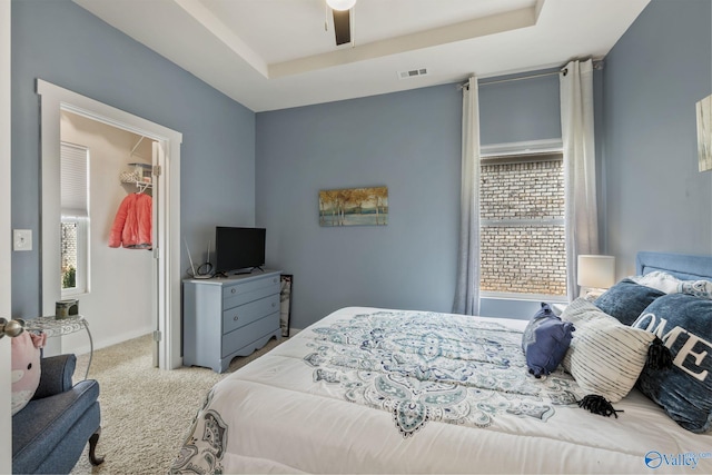 bedroom with visible vents, carpet, a raised ceiling, and a walk in closet