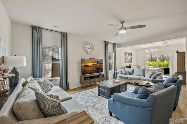 living area with light wood finished floors, baseboards, visible vents, and ceiling fan with notable chandelier