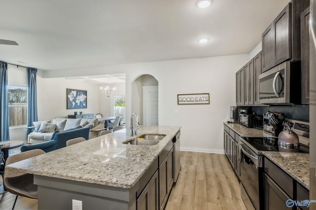 kitchen featuring stainless steel appliances, a sink, light wood-style floors, light stone countertops, and a center island with sink