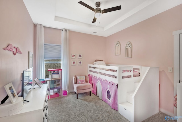 carpeted bedroom featuring a tray ceiling and ceiling fan