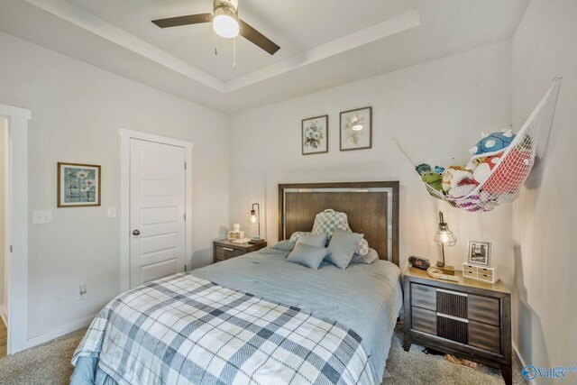 carpeted bedroom featuring a tray ceiling, ceiling fan, and baseboards