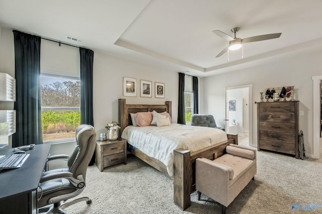 bedroom with carpet floors, a tray ceiling, visible vents, and a ceiling fan