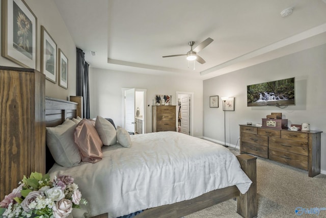 carpeted bedroom with a tray ceiling, connected bathroom, a ceiling fan, and baseboards