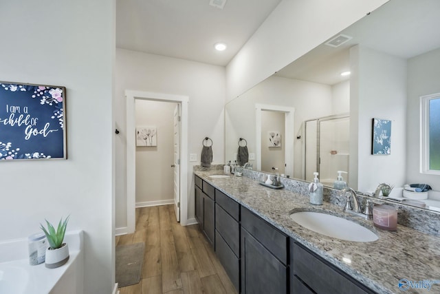 bathroom with wood finished floors, a sink, visible vents, a shower stall, and double vanity