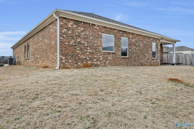 view of side of home with brick siding, fence, a lawn, and central AC unit