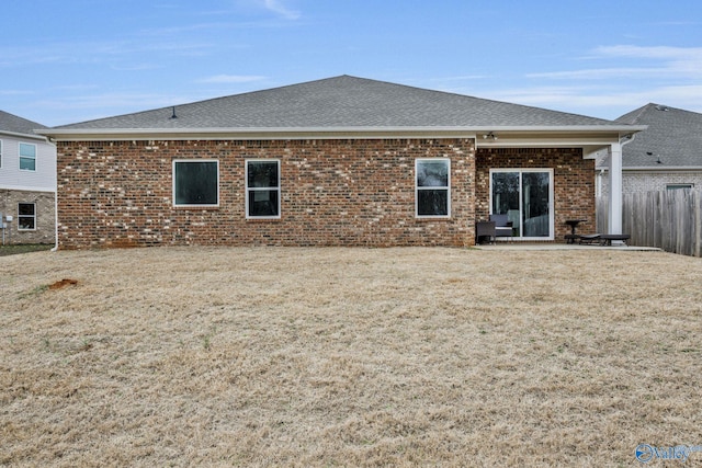 rear view of house featuring brick siding, a yard, fence, and roof with shingles