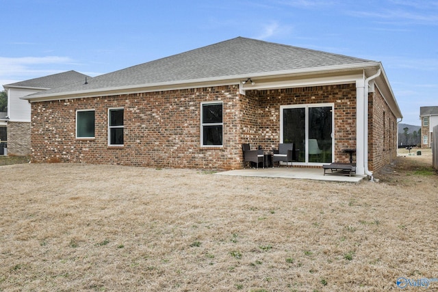 back of property featuring brick siding, a lawn, a patio area, and a shingled roof