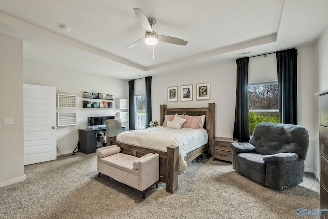 carpeted bedroom featuring a ceiling fan, a tray ceiling, and baseboards