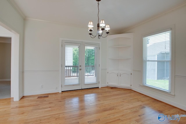 unfurnished dining area with french doors, crown molding, light wood finished floors, built in shelves, and a chandelier