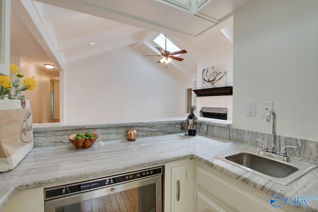 kitchen featuring a sink, wine cooler, a ceiling fan, a large fireplace, and light countertops