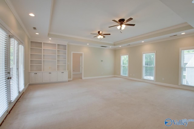 spare room with a tray ceiling, light carpet, healthy amount of natural light, ornamental molding, and baseboards