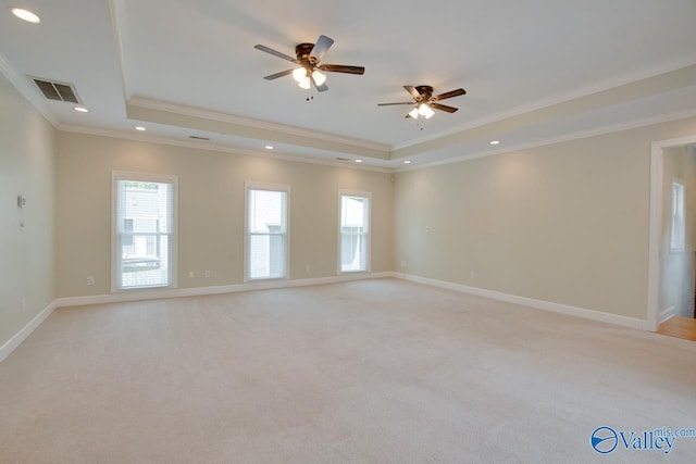 unfurnished room with a raised ceiling, ornamental molding, a ceiling fan, light colored carpet, and baseboards
