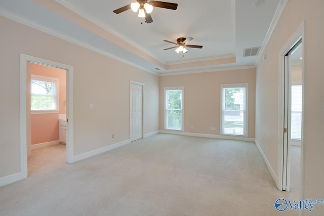 empty room featuring ceiling fan, a raised ceiling, light colored carpet, ornamental molding, and plenty of natural light