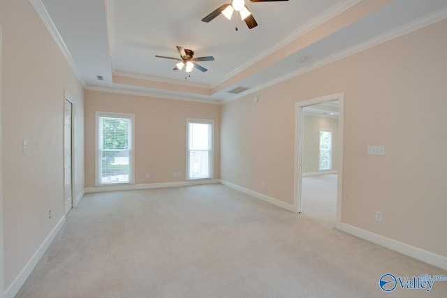 empty room with ceiling fan, crown molding, a tray ceiling, light colored carpet, and baseboards