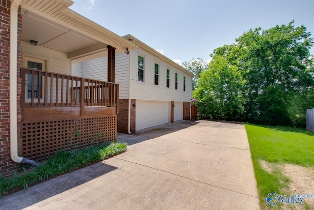 view of side of property with brick siding, an attached garage, driveway, and a yard