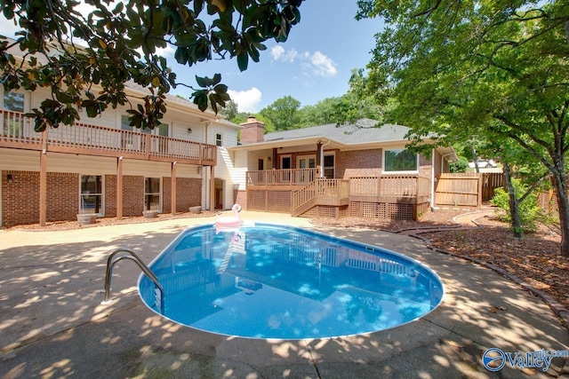 outdoor pool with fence, a wooden deck, stairs, and a patio