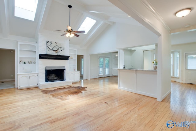 unfurnished living room featuring a skylight, a brick fireplace, light wood-style flooring, built in shelves, and high vaulted ceiling