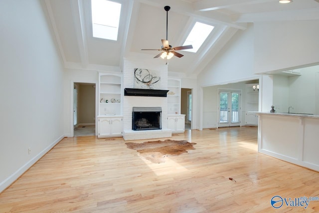 unfurnished living room with a skylight, a brick fireplace, a ceiling fan, beamed ceiling, and high vaulted ceiling