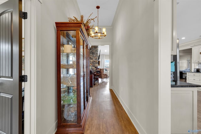 corridor featuring a chandelier, dark wood-type flooring, ornamental molding, and baseboards