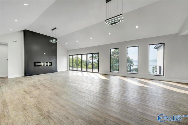 unfurnished living room with high vaulted ceiling, a large fireplace, light wood-style flooring, and baseboards