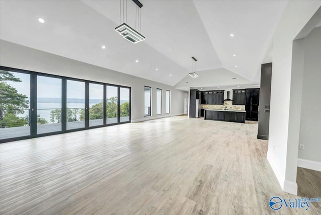 unfurnished living room featuring lofted ceiling, recessed lighting, a water view, light wood-style floors, and baseboards