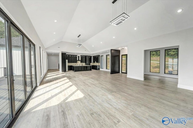 unfurnished living room with a healthy amount of sunlight, light wood-style floors, baseboards, and vaulted ceiling