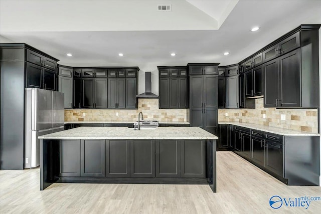 kitchen with light hardwood / wood-style floors, appliances with stainless steel finishes, decorative backsplash, and wall chimney range hood