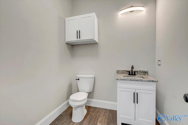 half bath featuring wood finished floors, vanity, toilet, and baseboards