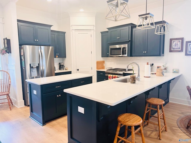 kitchen featuring appliances with stainless steel finishes, a breakfast bar, light wood-type flooring, decorative light fixtures, and sink