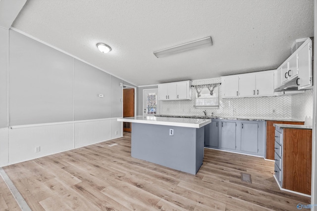 kitchen with white cabinets, light wood-type flooring, a textured ceiling, tasteful backsplash, and a kitchen island