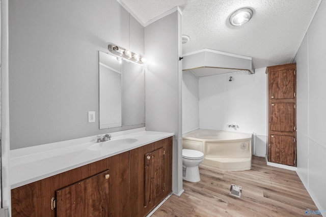 bathroom with a textured ceiling, vanity, a bath, hardwood / wood-style floors, and toilet