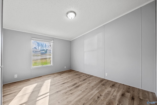 empty room with crown molding, light hardwood / wood-style floors, and a textured ceiling